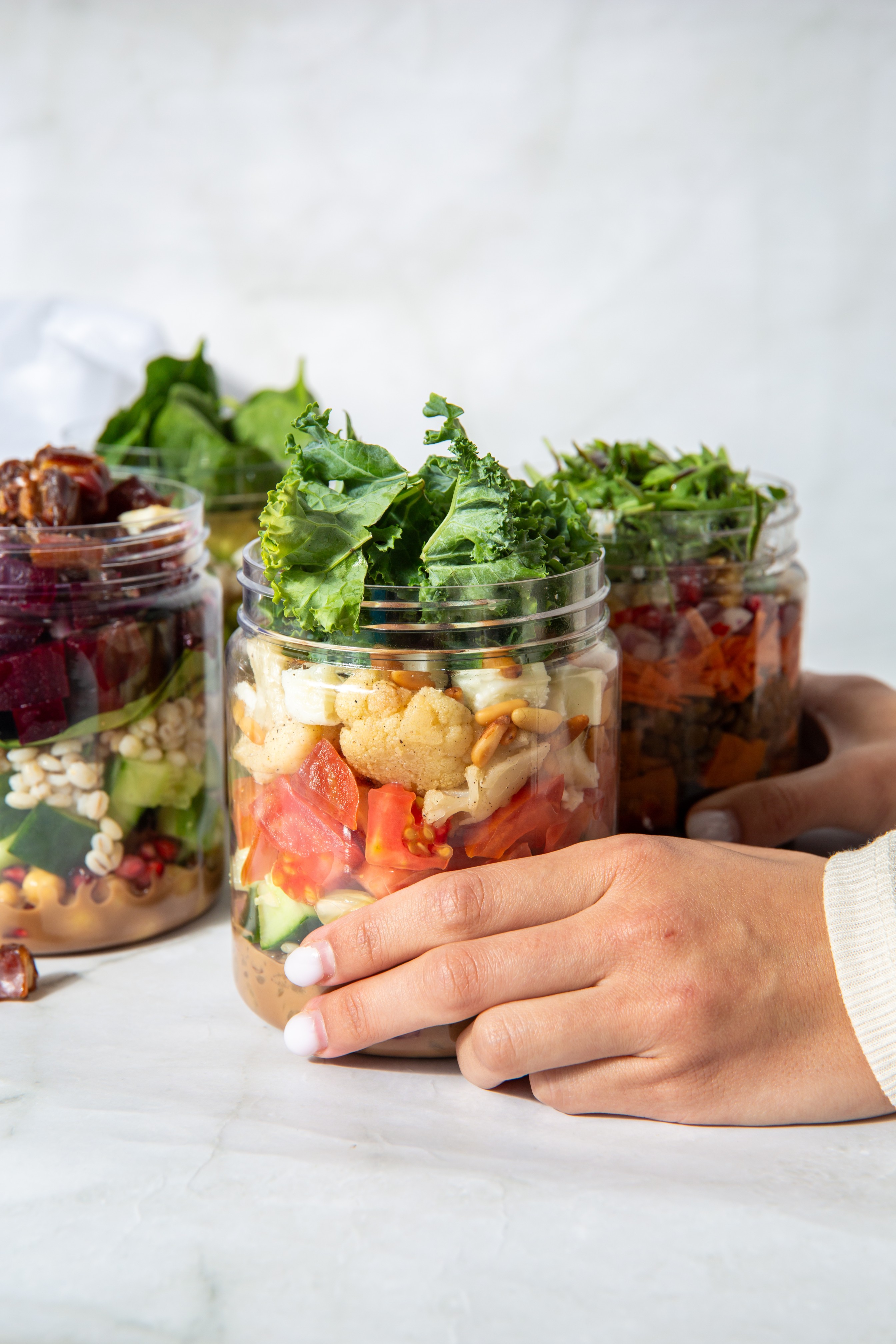 Hands holding Salad Jar salads on a marble counter